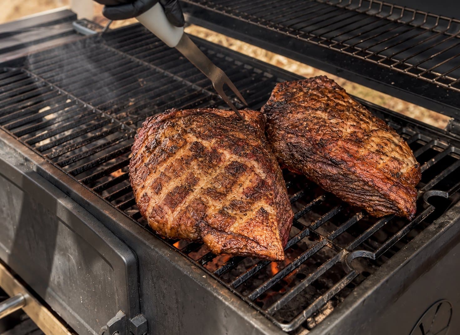 Two scored joints of beef searing on a charcoal barbecue grill